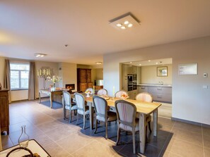 A spacious dining area with a wooden table and six chairs, a fireplace, and a kitchen visible through an open doorway.