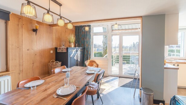 Un coin repas avec une table en bois, des chaises et une vue sur une terrasse extérieure, accessible par une porte vitrée.