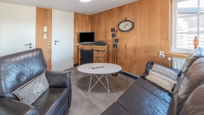 Un salon avec un canapé, une table basse, un téléviseur et une horloge au mur.