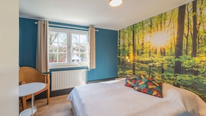 Une chambre à coucher comprenant un lit, une chaise, une table, une fenêtre et une fresque représentant une forêt sur le mur.