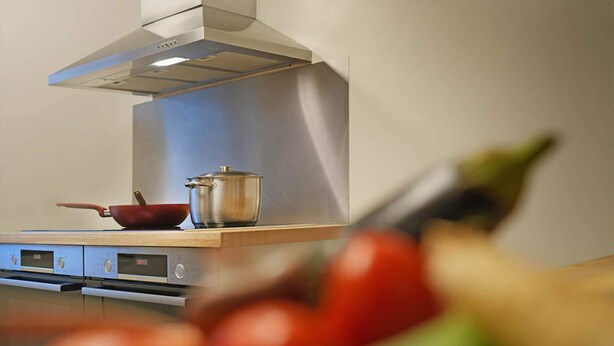Una cuina amb electrodomèstics d'acer inoxidable, una olla sobre el taulell i una paella.