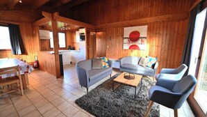 Un accogliente interno di una baita con pareti in legno, un'area pranzo, un soggiorno con divani e un tavolino, e una cucina sullo sfondo.