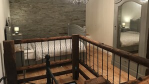 A bedroom with a stone wall, a wooden ceiling, a chandelier, a bed, a nightstand, and a mirror. - Peaceful Holiday Home With Garden in Fauvillers Belgium (Fauvillers)