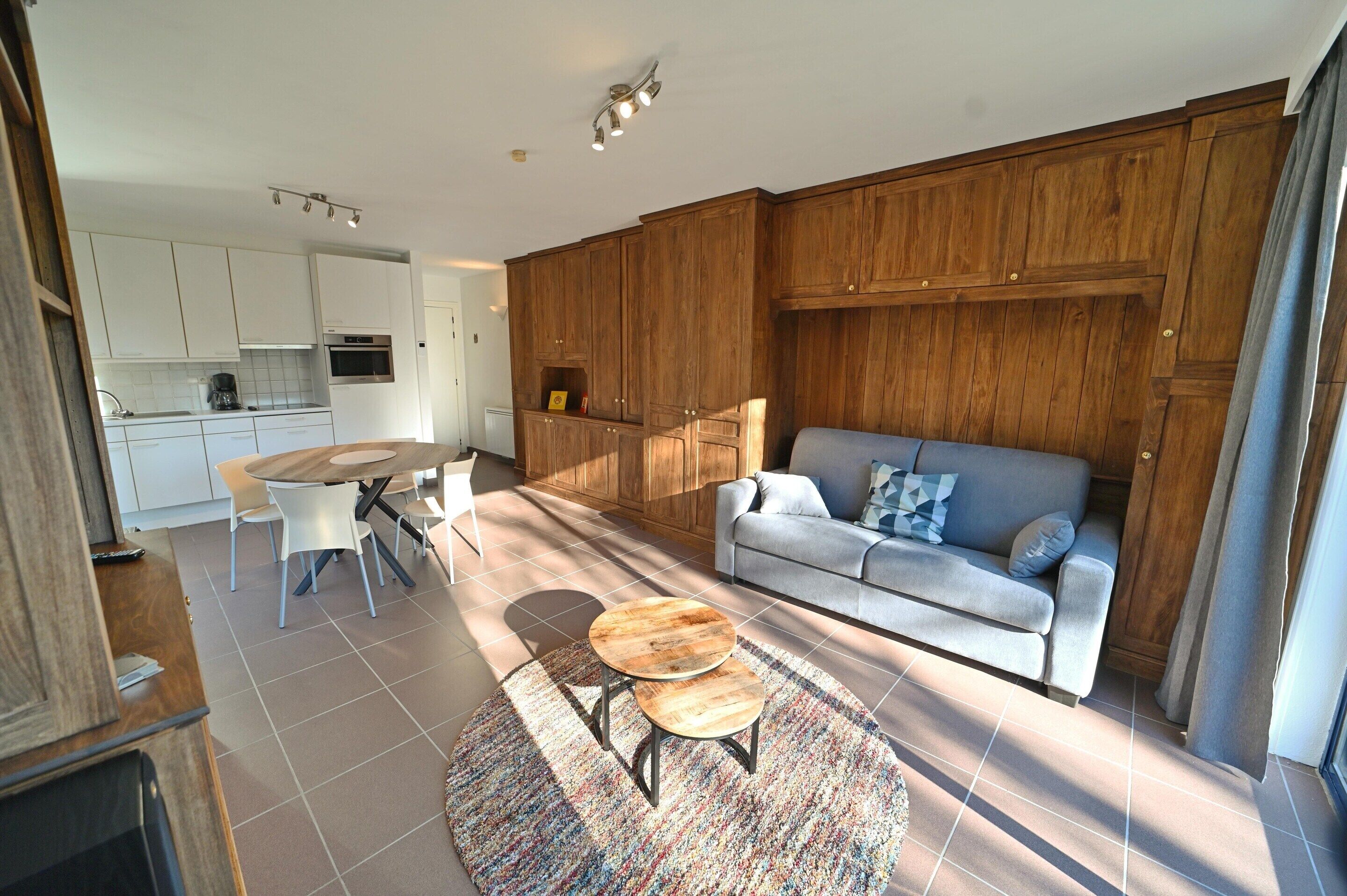 A modern kitchen with white cabinets, a dining area with a round table and chairs, and a living area with a sofa and a coffee table.
