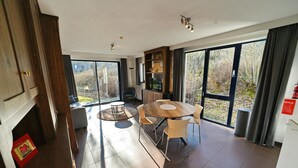 Et moderne spiseområde med et rundt bord og stole, et træskab og et stort vindue med udsigt over det fri.