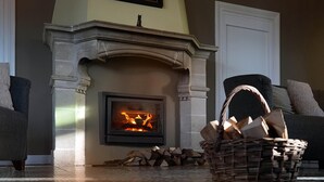 A fireplace with a fire, a wicker basket with firewood, and two sofas in a living room. - Chateau in Stavelot With Private Pool & Sauna (Stavelot)