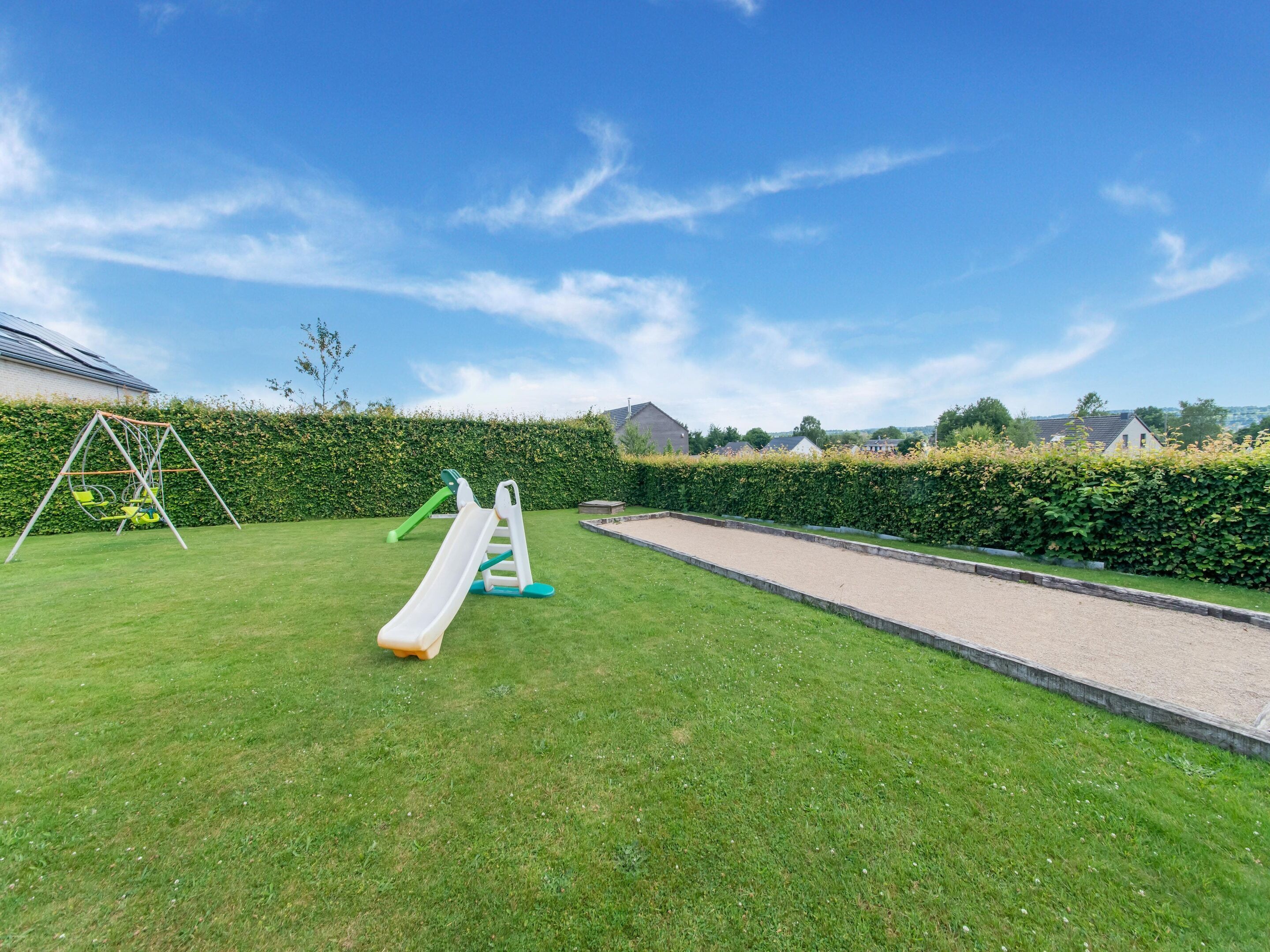 A grassy outdoor area with a swing set, a slide, and a croquet court.