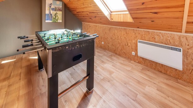 Una habitación con mesa de fútbol, paredes de madera, techo inclinado con tragaluz y radiador.