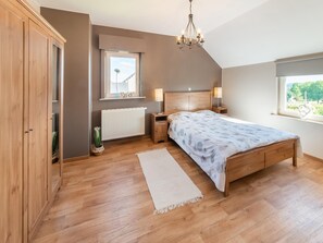 A bedroom with a wooden bed, a radiator, a window with a view, and a chandelier. - Detached House with Sauna & Hot Tub near Ski Resort & Nature Park (Waimes)