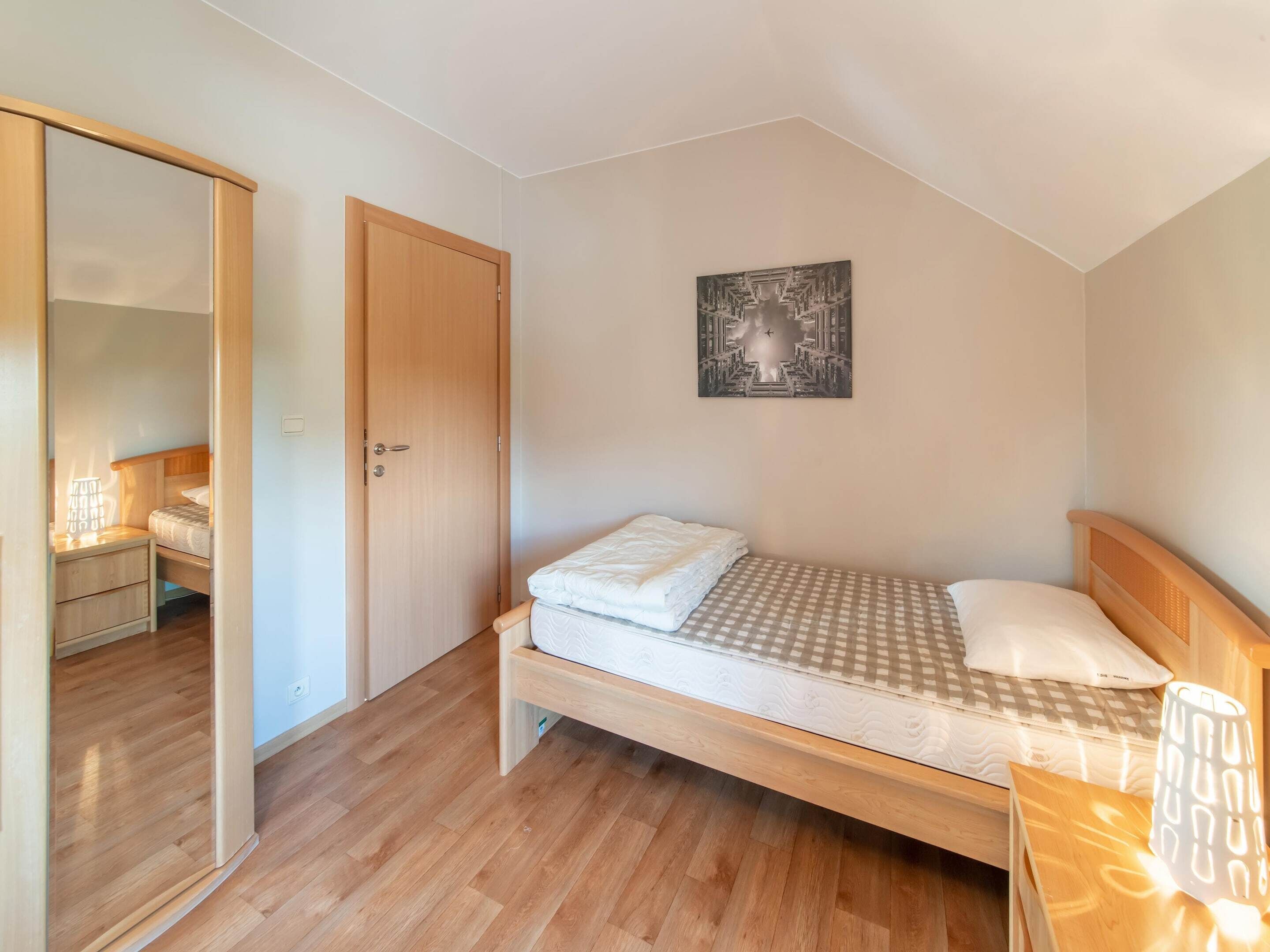 A bedroom with a wooden bed, a nightstand, a bedside table with a lamp, a wardrobe, and a painting on the wall.