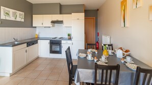 Una cocina moderna con armarios blancos, una estufa y un comedor con una mesa dispuesta para el desayuno.