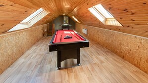 Una mesa de billar en una sala de madera con techos inclinados y tragaluces.