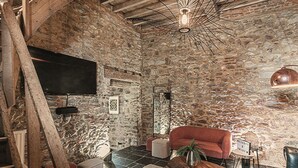 A rustic stone-walled room with a modern sofa, a wooden coffee table, and a television mounted on the wall. - Castle Farmhouse in Condroz With Heated Pool (Ohey)