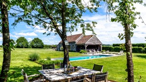 A wooden table with chairs set outdoors, a swimming pool, and a house with a tiled roof in the background. - Castle Farmhouse in Condroz With Heated Pool (Ohey)