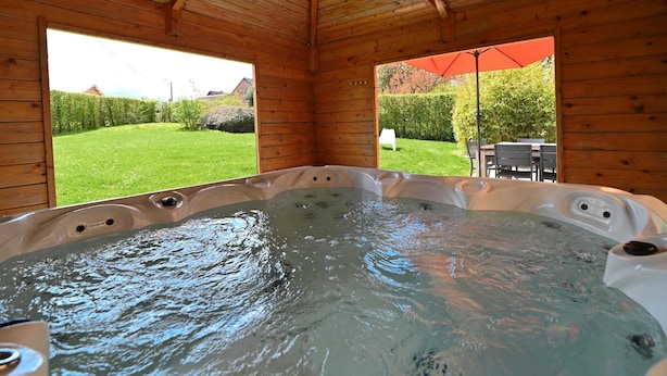 Eine Holzhütte mit Whirlpool, großen Fenstern und Blick auf einen grünen Garten.