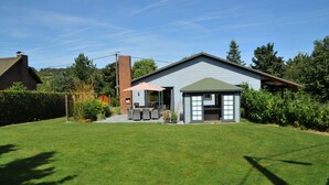 Ein Haus mit einer Terrasse, einem Schornstein und einem gepflegten Rasen.