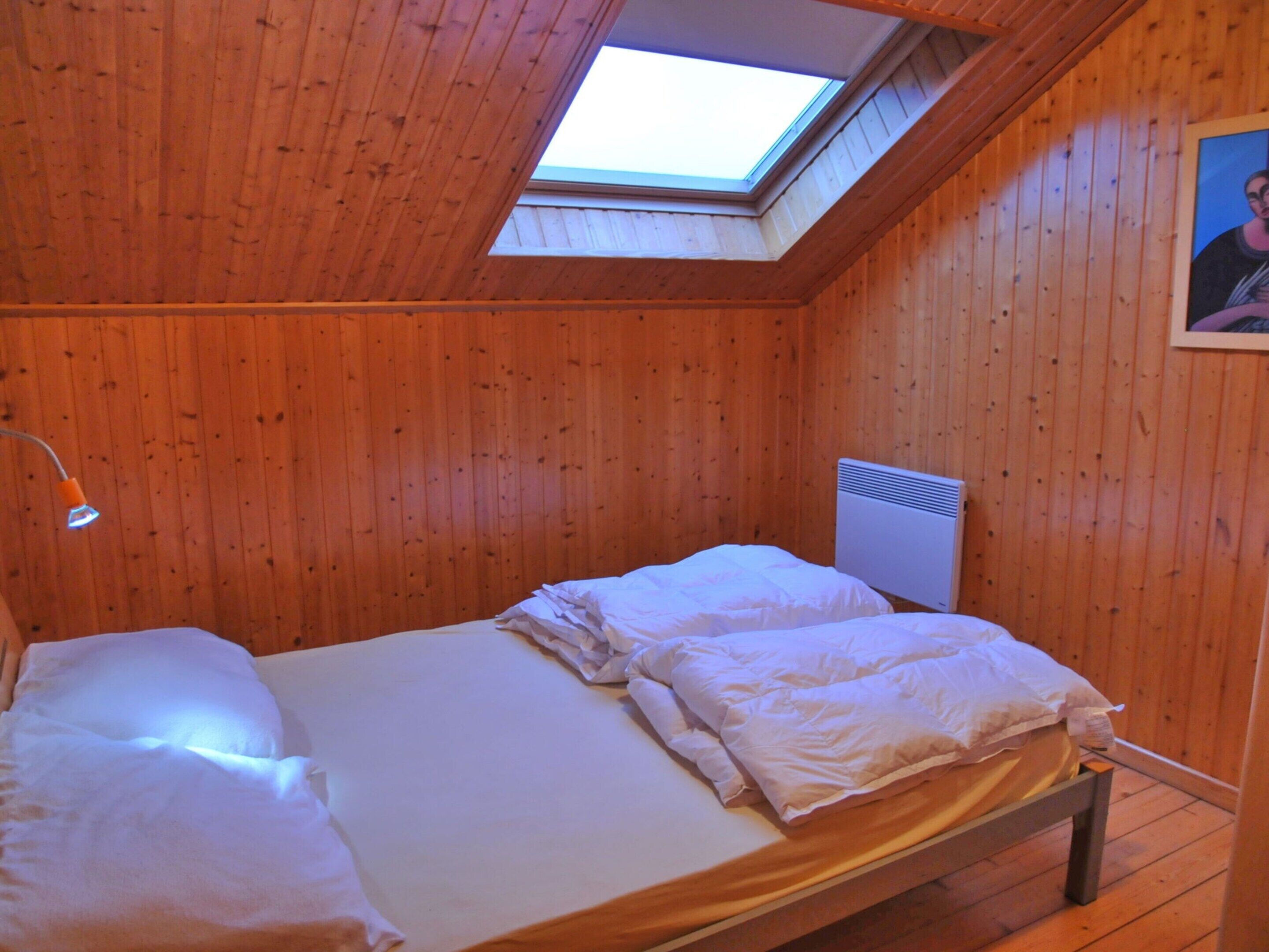 A single bed in a wooden room with a skylight.