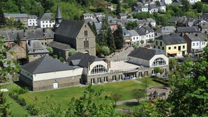 A town with a prominent church, a large building with a curved roof, and surrounding residential houses. - Holiday Home in Houffalize Near Nisramont (Houffalize)