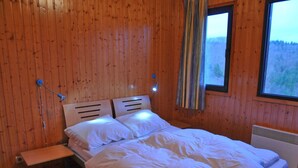 A wooden-paneled room with a bed, a nightstand, and a window with curtains. - Holiday Home in Houffalize Near Nisramont (Houffalize)
