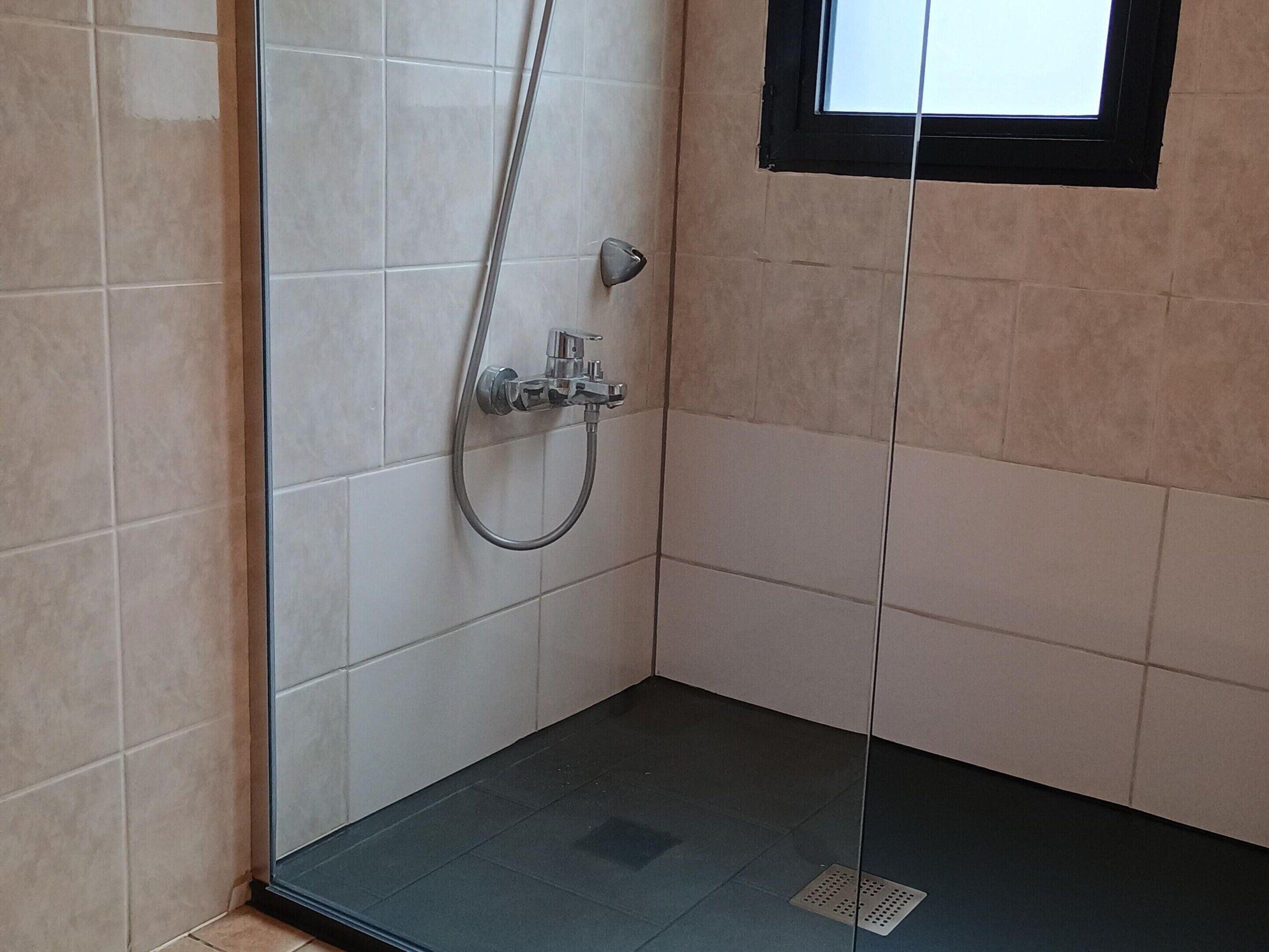 Ein kleines Duschbad mit gefliesten Wänden, einer Glastür und einem Fenster darüber.