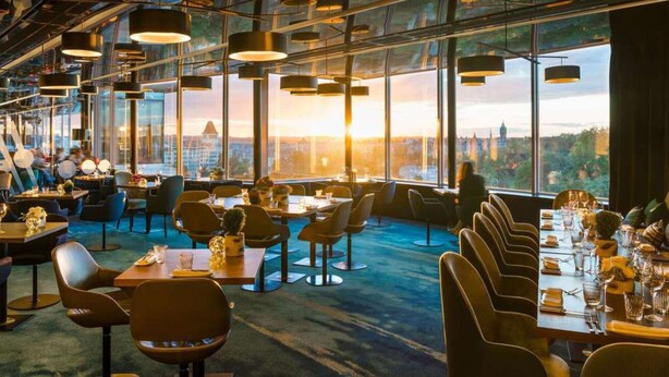A modern restaurant with high ceilings, large windows, and a city view. Tables are set with chairs, and the interior has a contemporary design. - Holiday Home in Houffalize Near Nisramont (Houffalize)