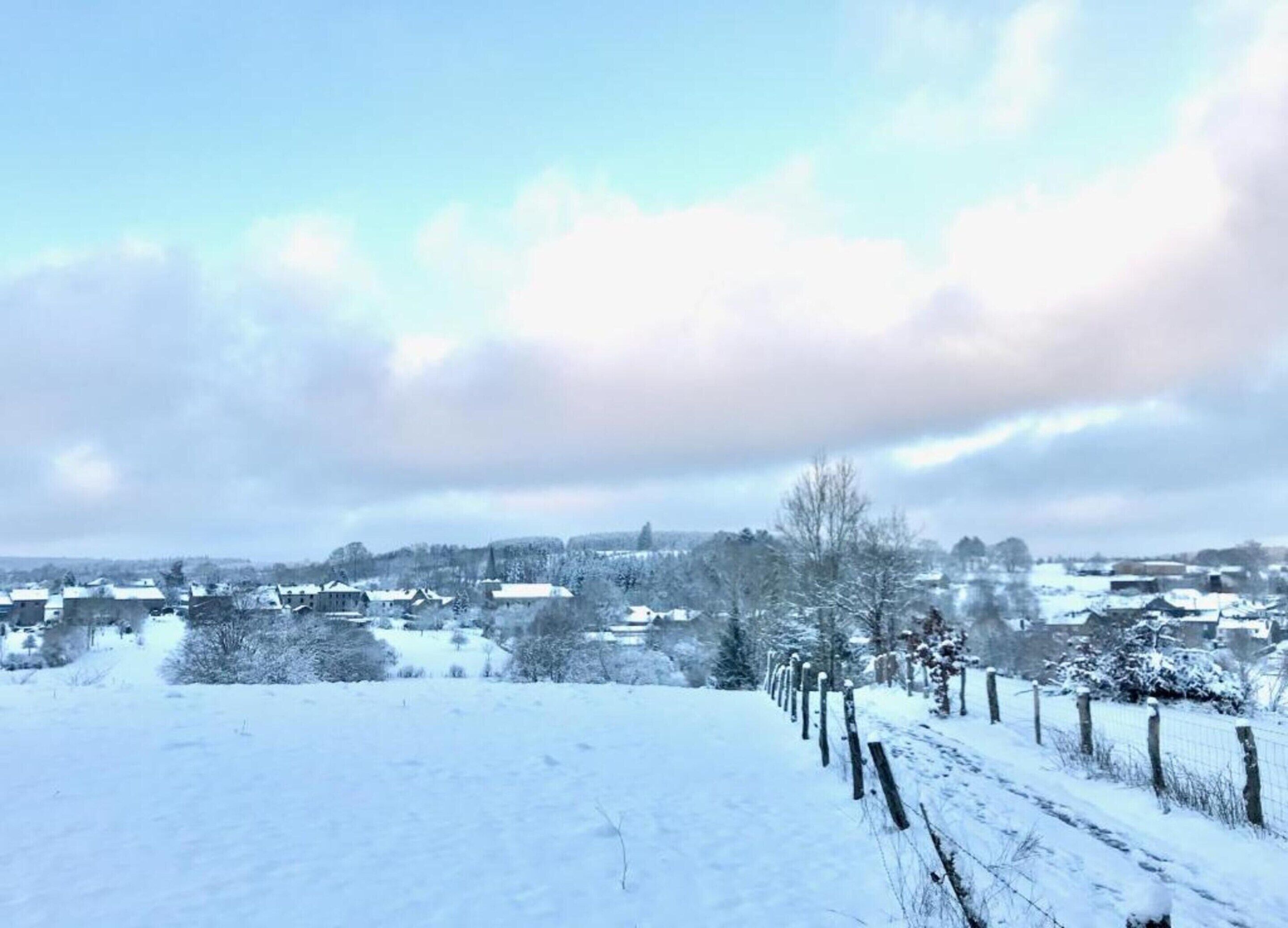 Paisaje nevado con una cerca y casas al fondo.