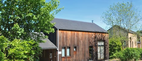 A modern wooden building with a sloped roof, a gated entrance, and a small parking area.