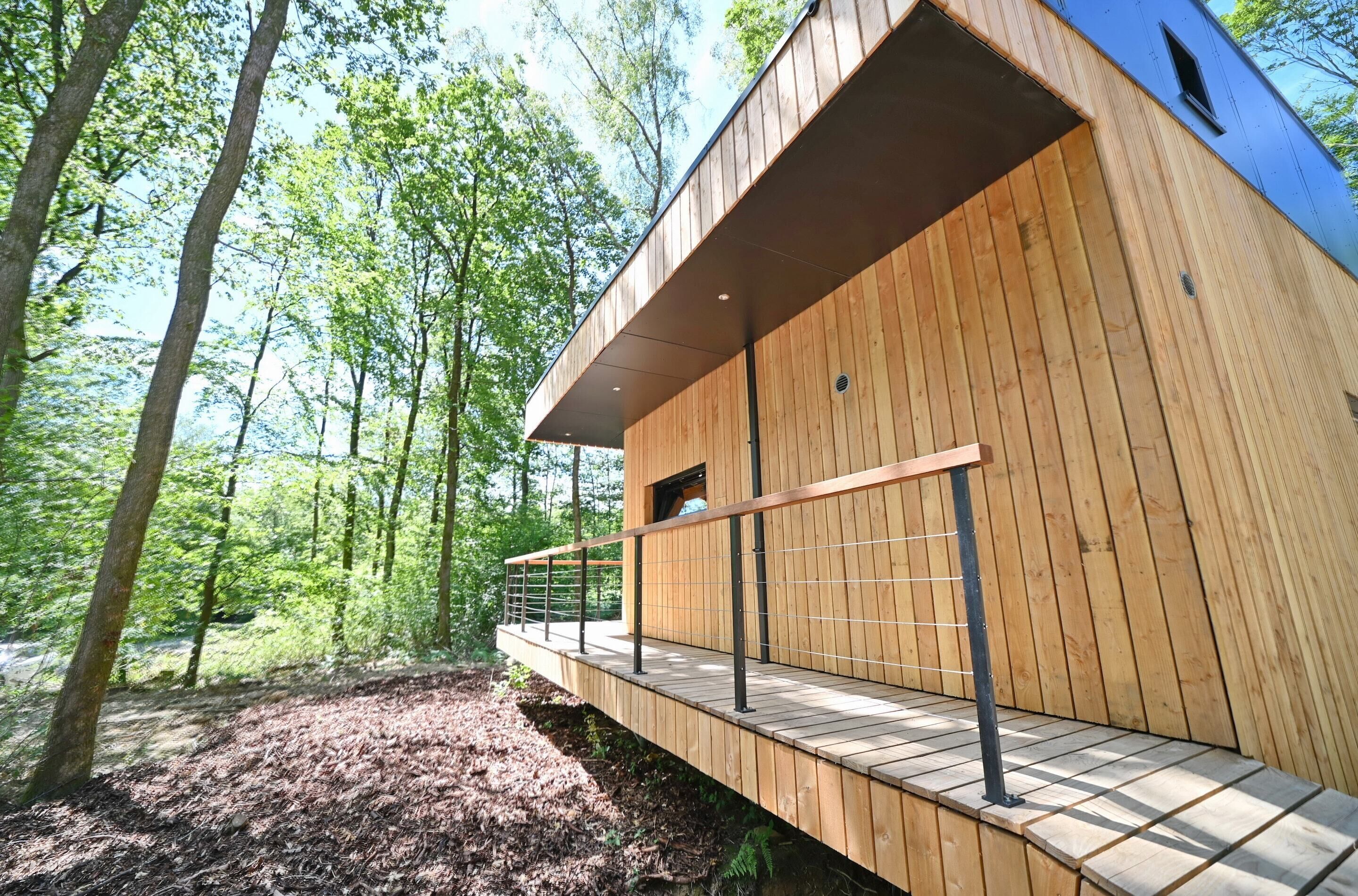 Una cabaña moderna de madera con balcón, rodeada de un bosque.