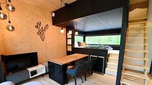 A compact, modern room with a wooden floor, a desk, a chair, a sofa, and a bed with a view. - Lodge in Oignies Forest With Eco Design (Viroinval)