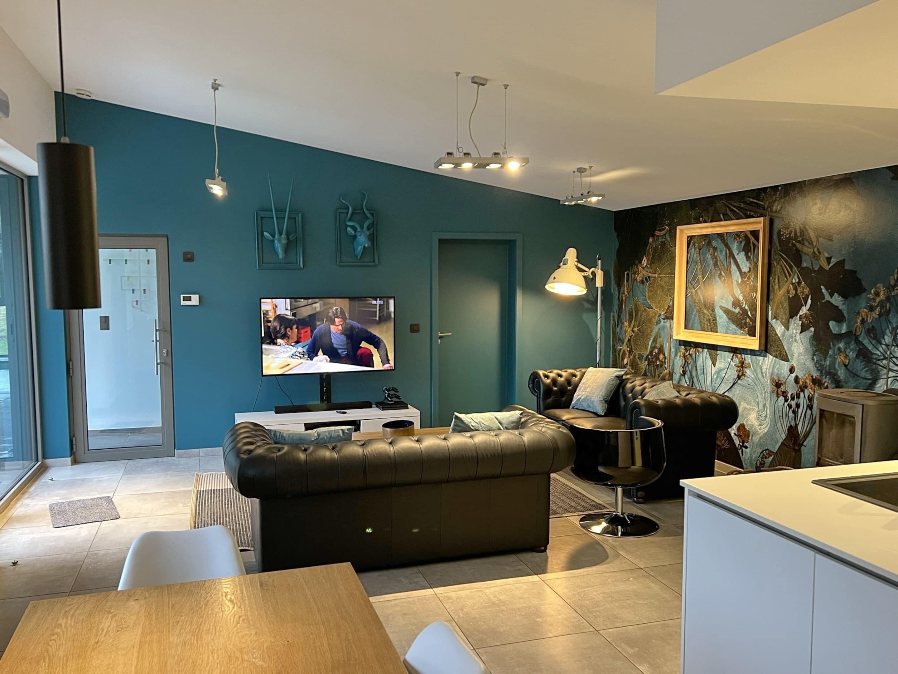 A modern living room with a television, leather sofa, dining table, and a kitchen area.