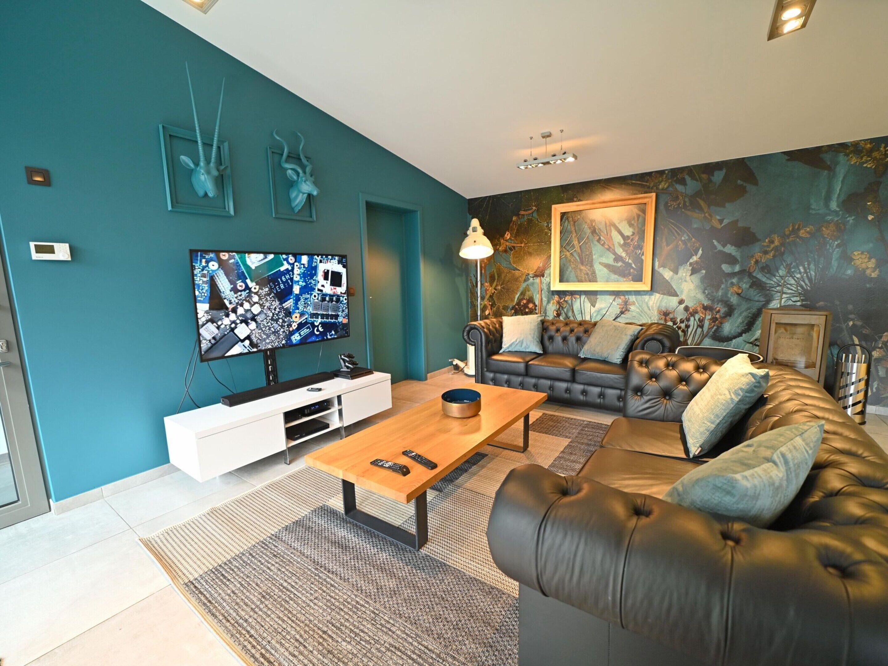 A modern living room with a teal accent wall, a flat-screen TV, a leather sofa, and a coffee table.