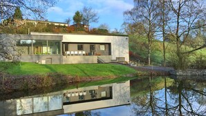 A modern house with a glass facade, a small deck, and a reflection in the water. - Holiday Home in Noiseux With Indoor Pool (Somme-Leuze)
