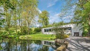 A modern house with a pond in front, surrounded by trees and greenery. - Holiday Home in Noiseux With Indoor Pool (Somme-Leuze)
