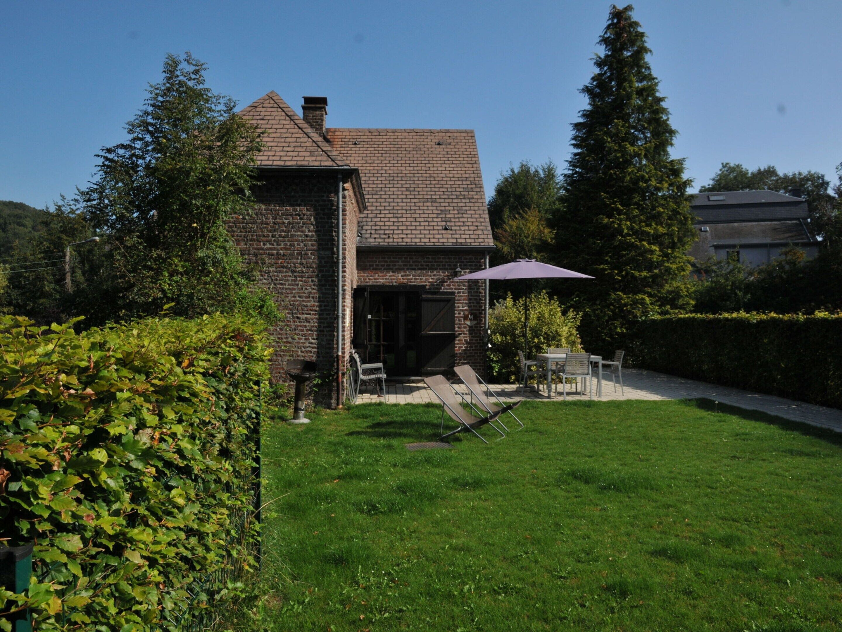 A brick house with a covered patio, a lawn, and a hedge.