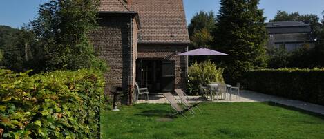 A brick house with a covered patio, a lawn, and a hedge.