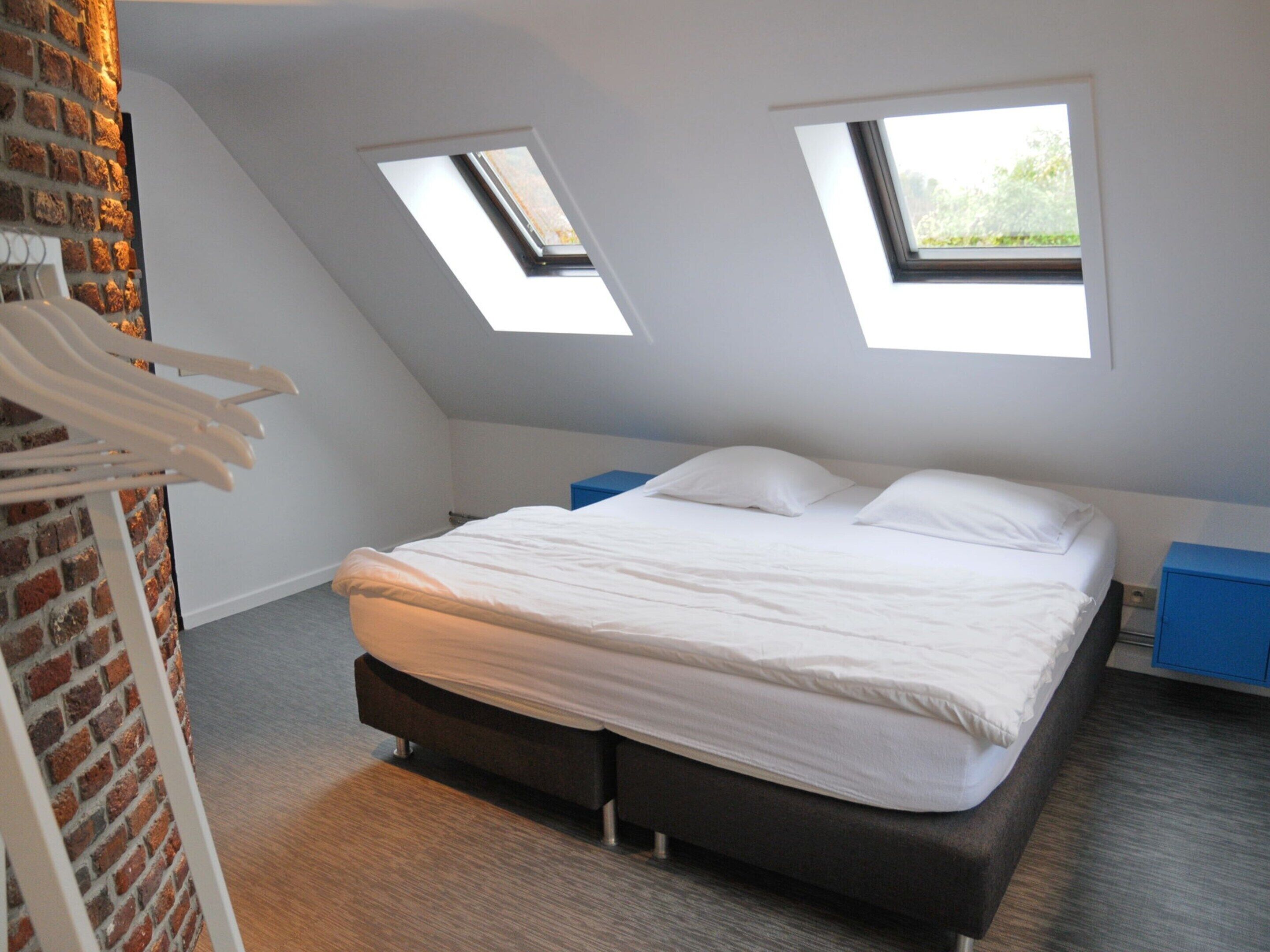 A bedroom with a bed, two skylights, a brick wall, and a wooden floor.