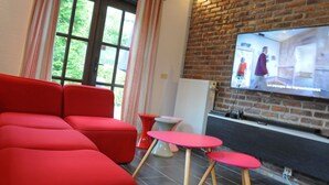 Ein modernes Wohnzimmer mit roter Möbel, einer Ziegelwand und einem Fernseher, der eine Szene zeigt.