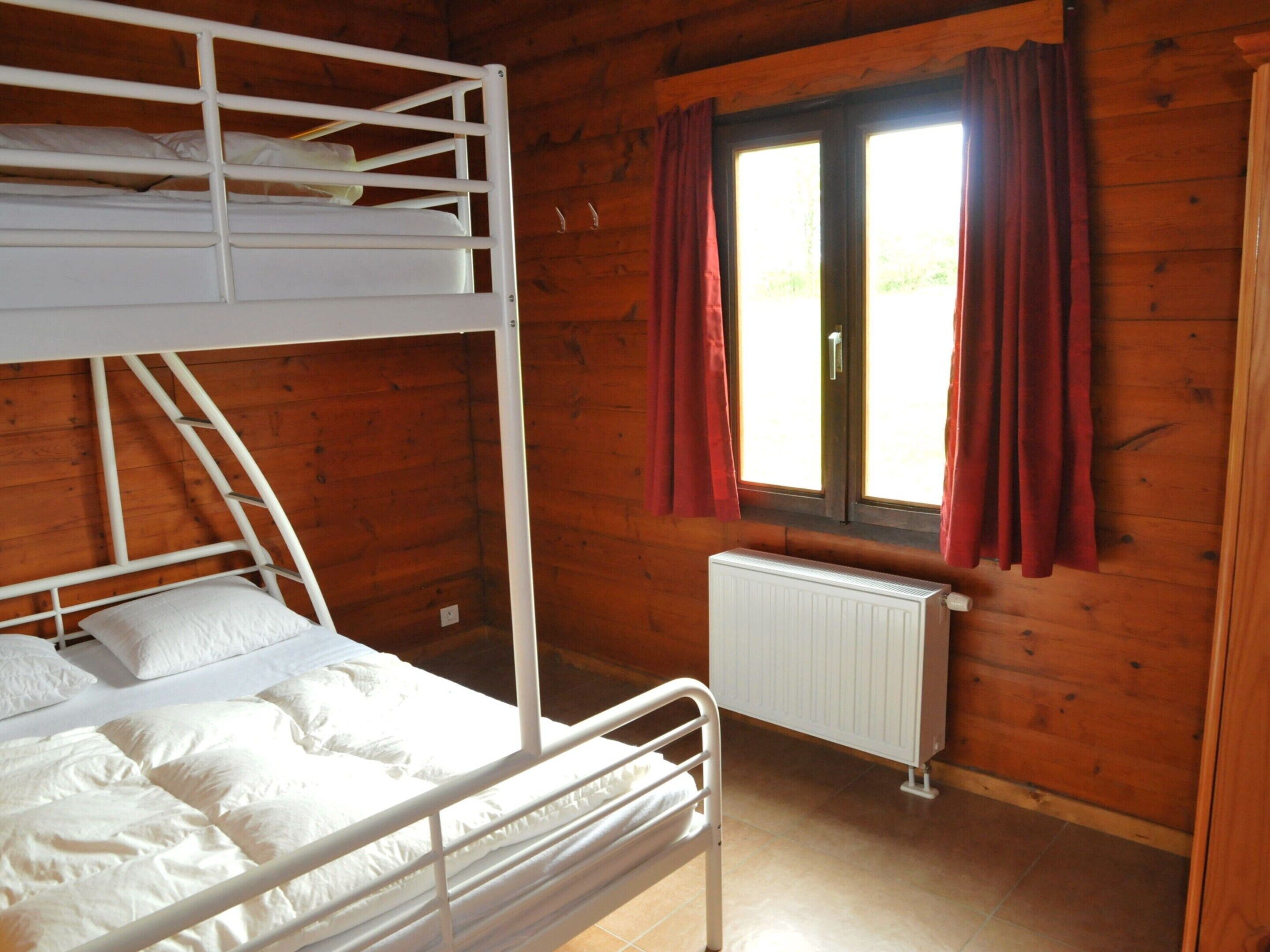 A bunk bed room with a window and curtains, wooden walls, and a radiator.