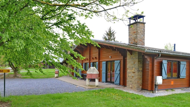 A lodge with a stone chimney, wooden exterior, and a covered outdoor seating area. - Holiday Home in Houyet With Sauna & Garden (Houyet)