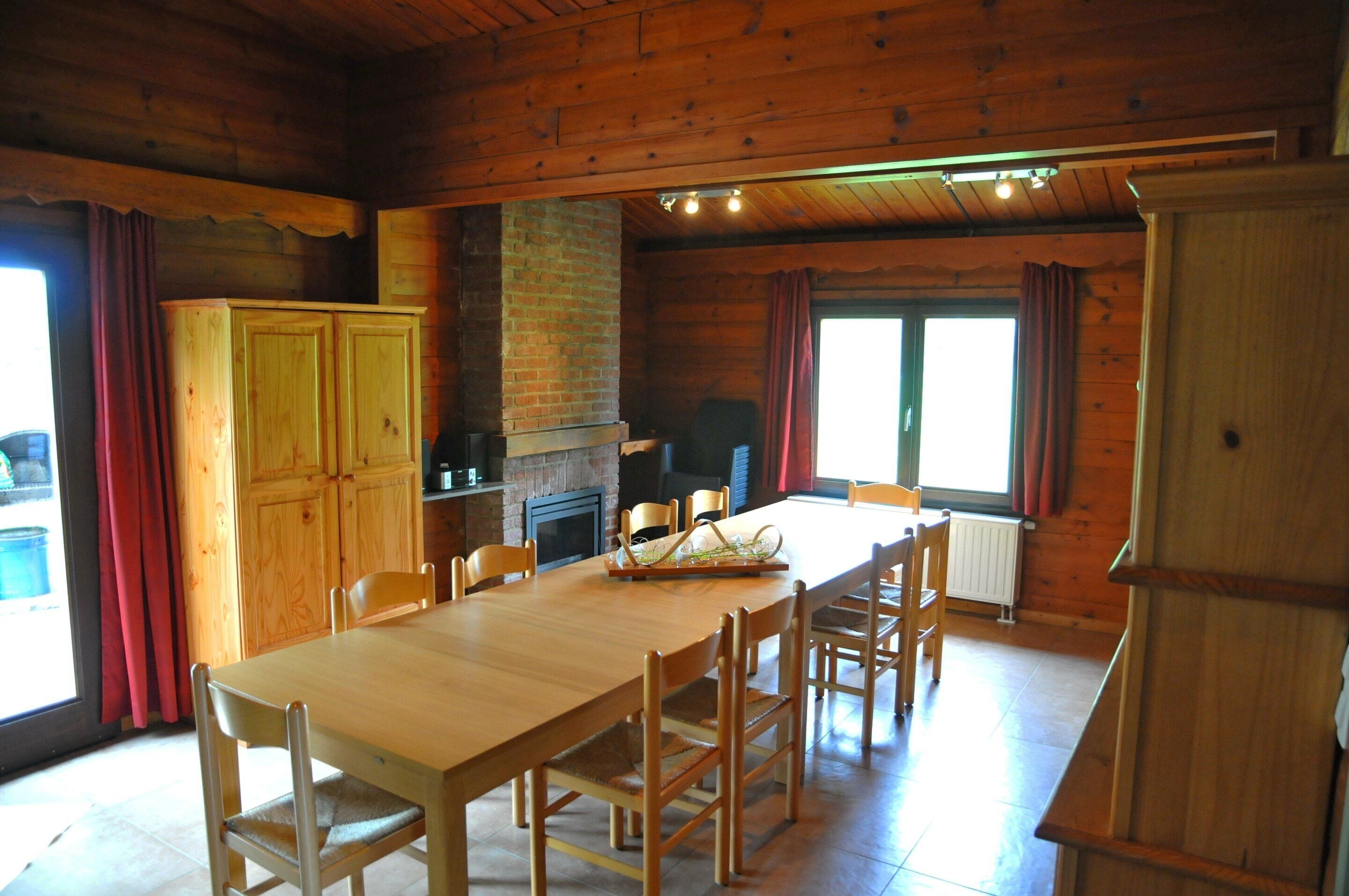 A wooden interior with a dining table, chairs, a fireplace, and a kitchen area.