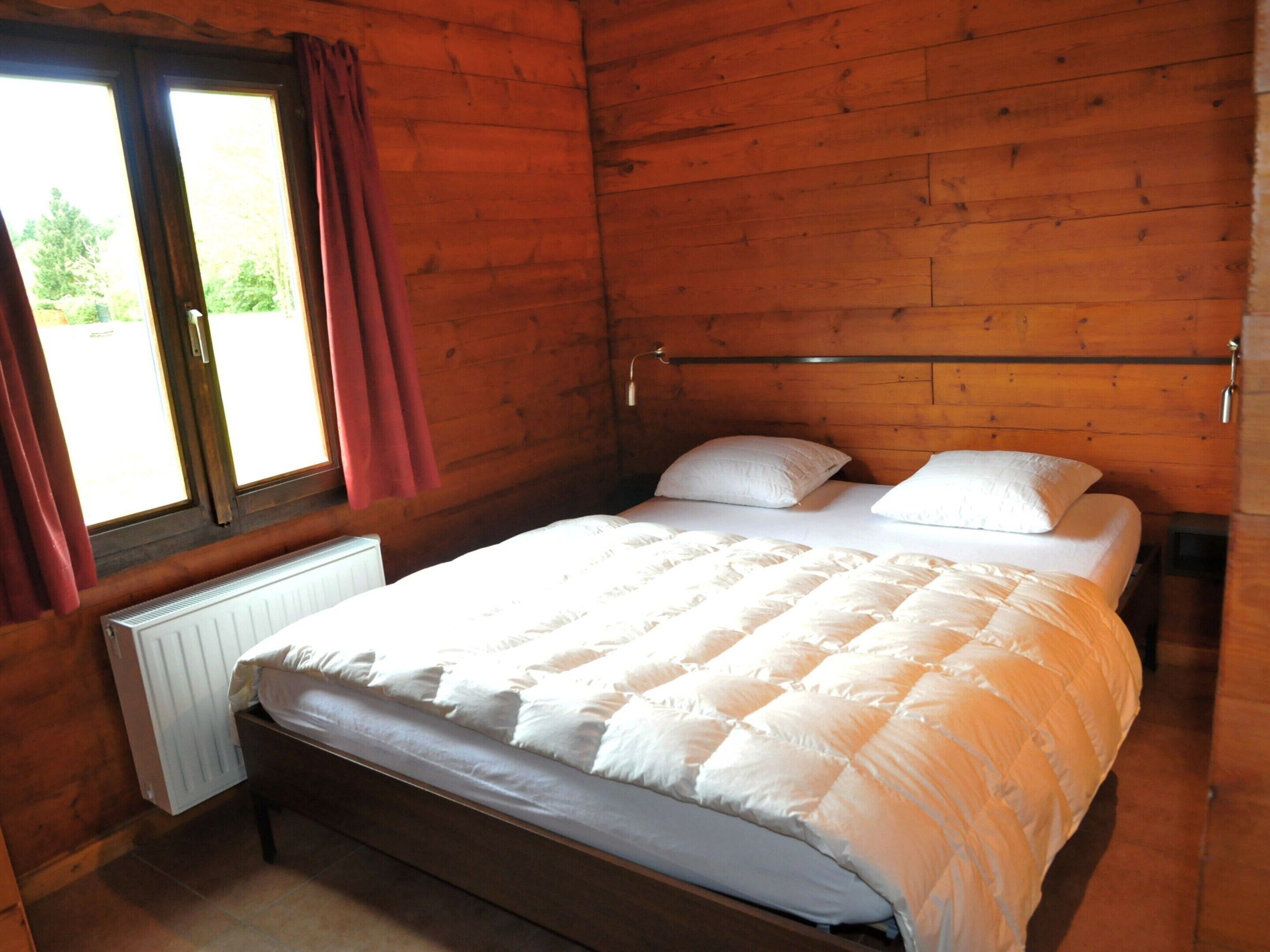 Ein Schlafzimmer mit Holzwänden, einem Einzelbett, einem Fenster mit Vorhängen und einer Heizung.