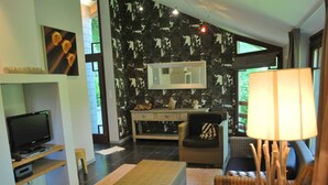 A modern living room with a flat-screen TV, wicker furniture, a large mirror, and a view of greenery outside. - Cozy Holiday Home in Durbuy With Garden (Durbuy)
