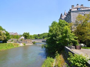 A river with a stone bridge, a stone building with a tower, and lush greenery along the riverbank. - Holiday Home in Durbuy With Garden & BBQ (Durbuy)