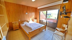A wooden-paneled bedroom with a single bed, a nightstand, a chair, and a sliding glass door to a balcony. - Holiday Home in Durbuy With Garden & BBQ (Durbuy)