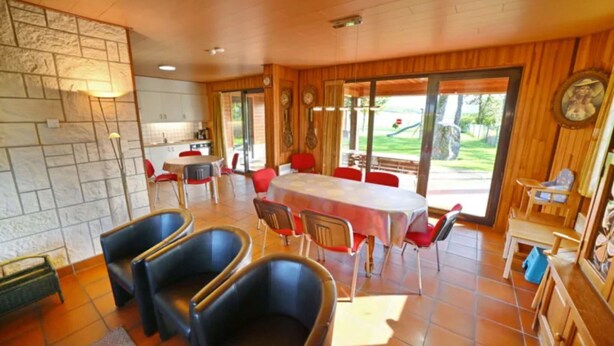 A dining area with a large table and chairs, a kitchen in the background, and a view of the outdoors. - Holiday Home in Durbuy With Garden & BBQ (Durbuy)
