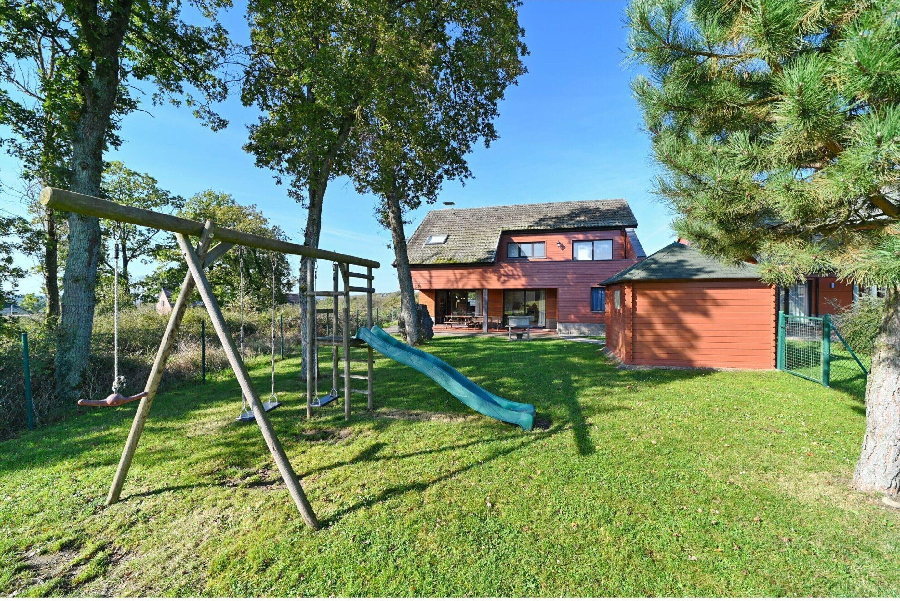 A residential property with a backyard featuring a swing set and a slide, a red house, and a fenced area.