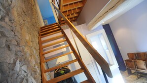 A wooden staircase with a stone wall on one side, leading to a room with a door and a chair.