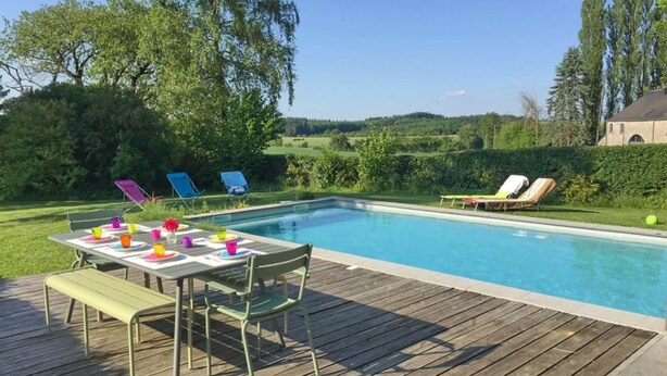 A swimming pool with a wooden deck, lounge chairs, and a table with colorful cups.