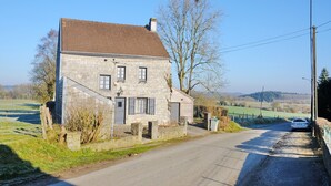 A stone house with a sloped roof, a small porch, and a car parked in front.
