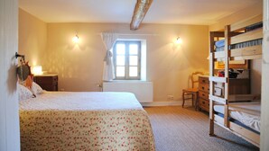 A bedroom with a single bed, a wooden bunk bed, a radiator, a window with curtains, a chair, and a dresser.